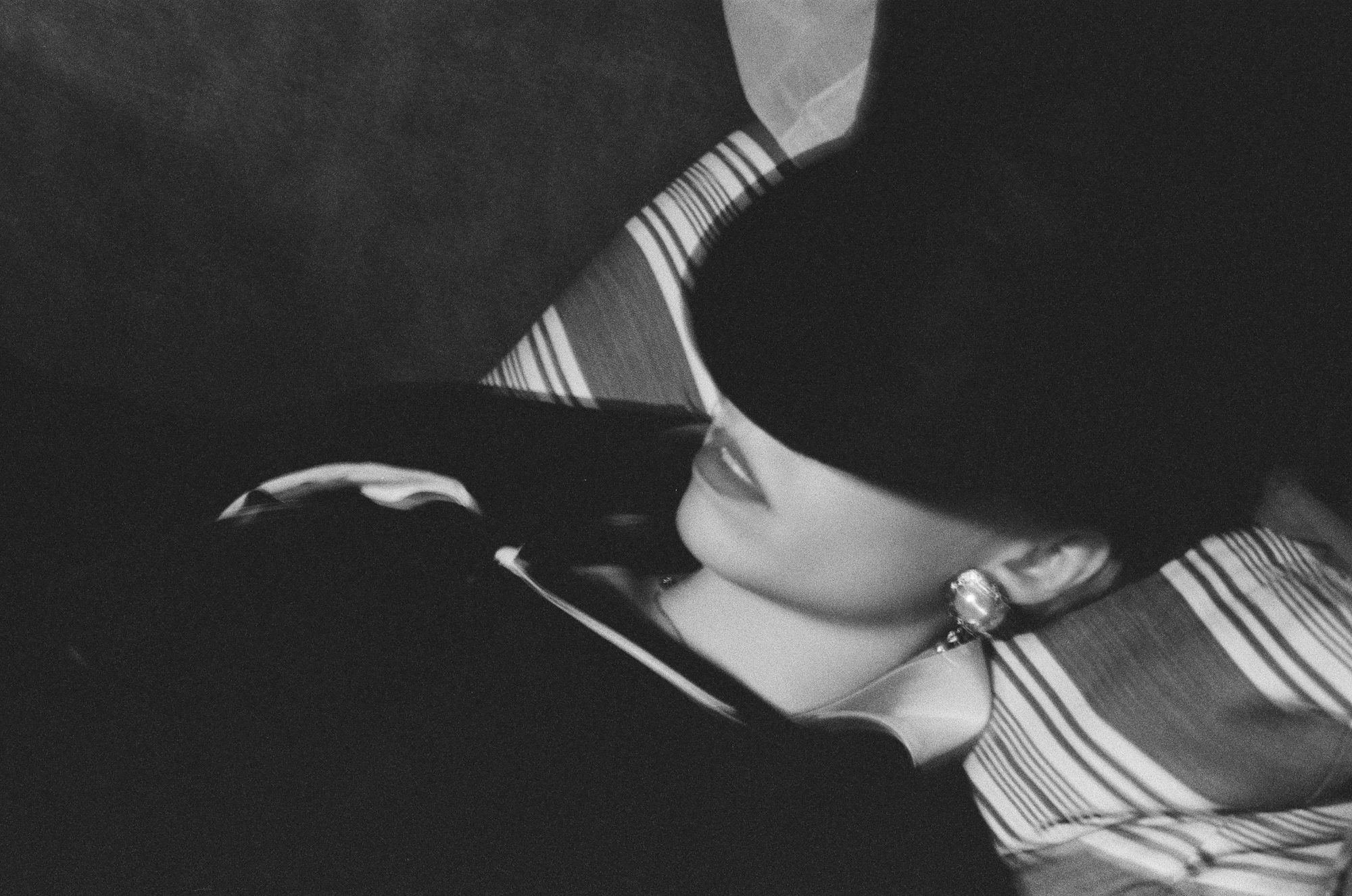 Black and white portrait of a woman in a wide-brimmed hat, face half in shadow, striped light across her collar