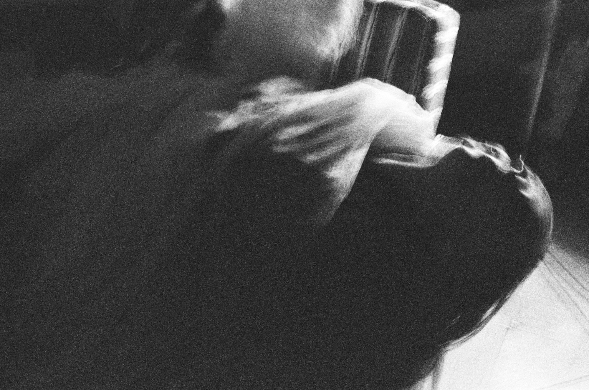 Black and white motion blur of a figure in a white dress spinning beside a striped armchair