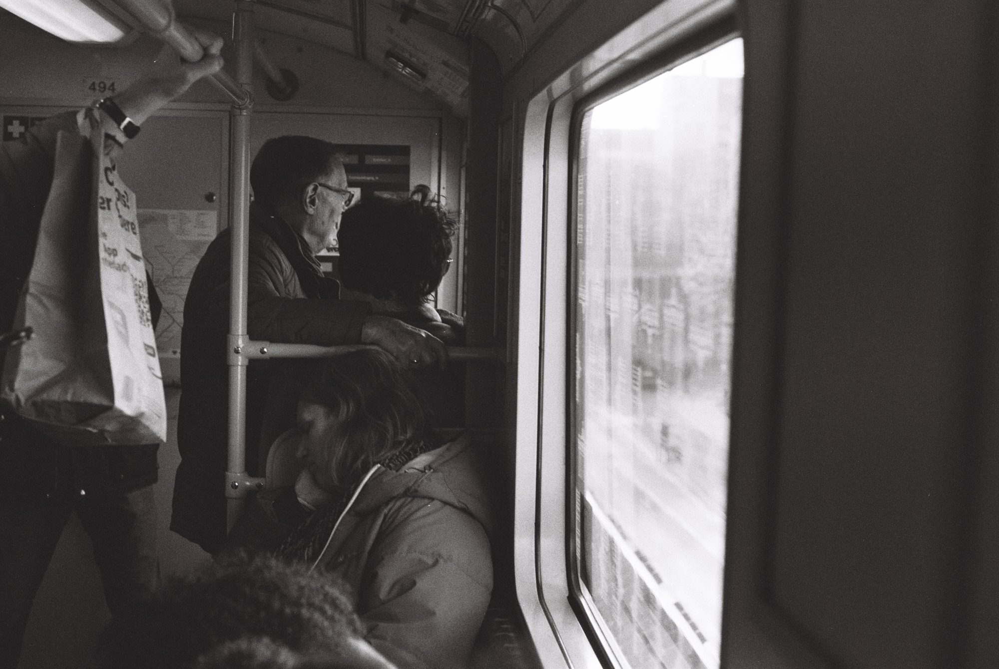 Black and white view inside a Berlin train carriage, passengers by the window as the city passes outside