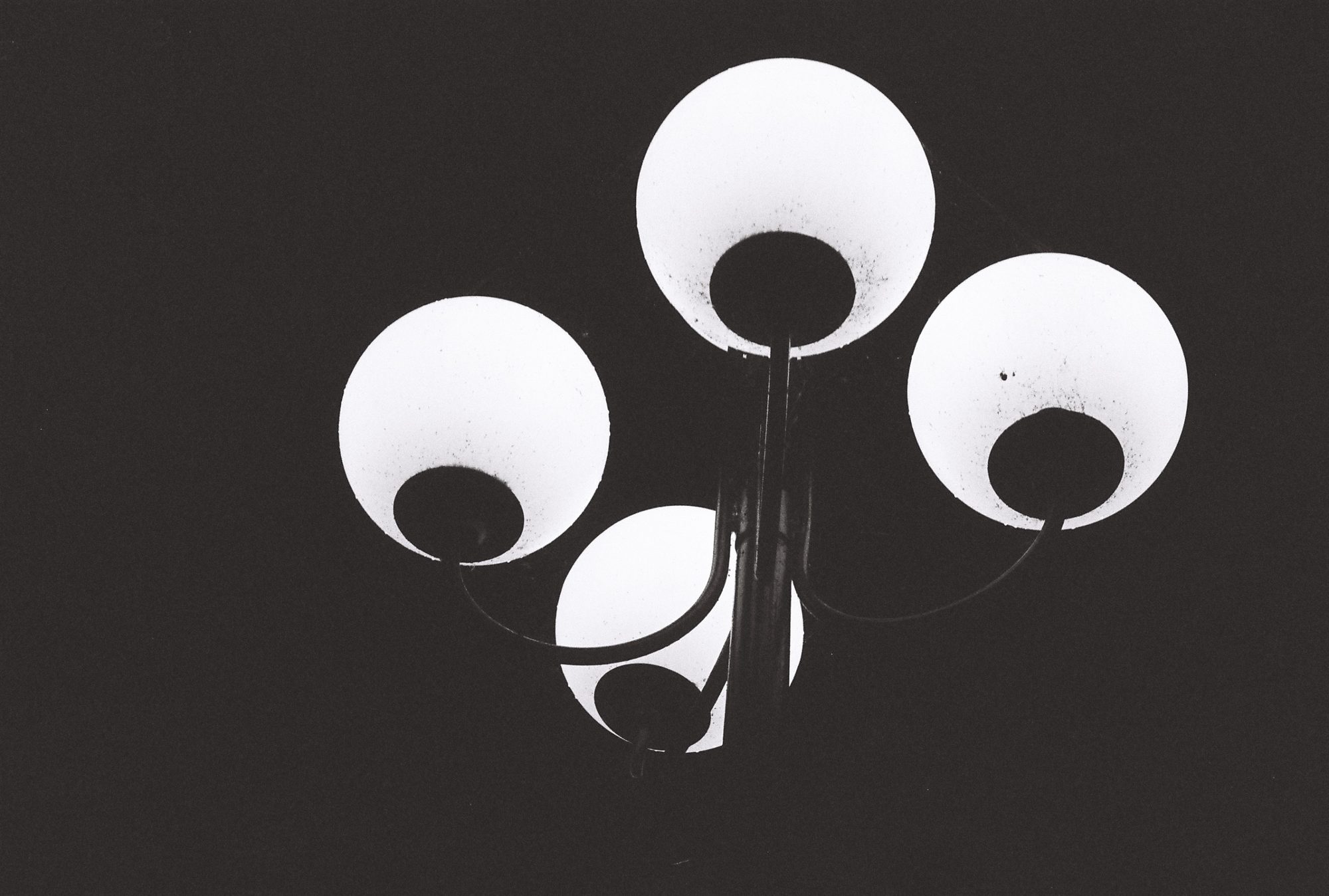 Four glowing globe street lamps against a black night sky, in black and white