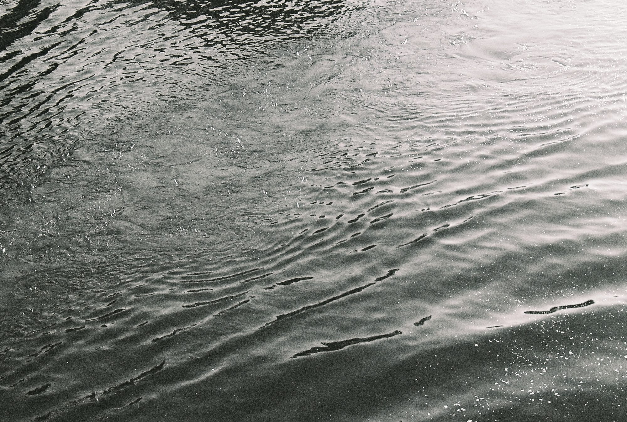 Black and white close-up of rippling water surface with glinting light