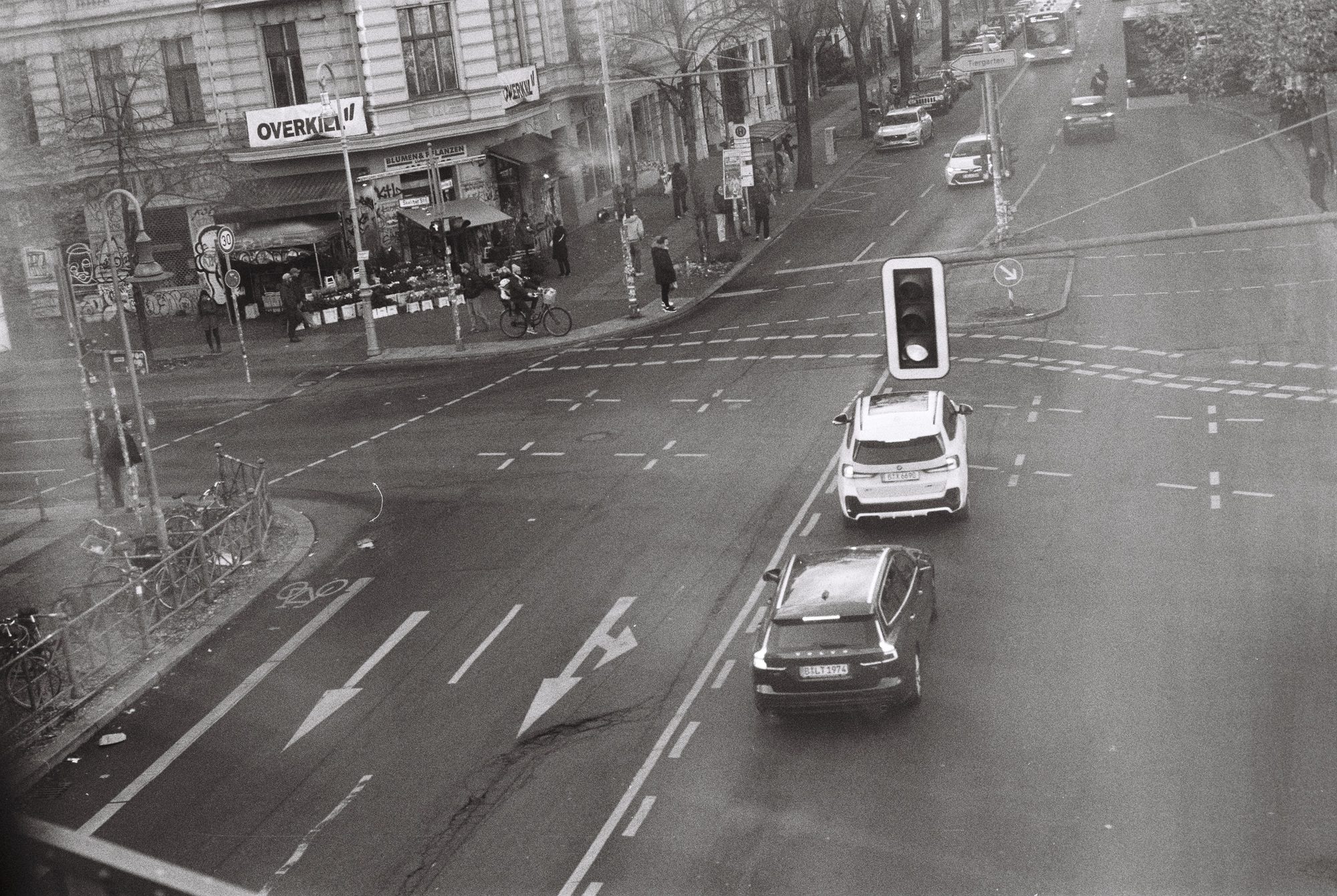 Black and white view from above of a Berlin street corner, cars at a traffic light and a flower stall