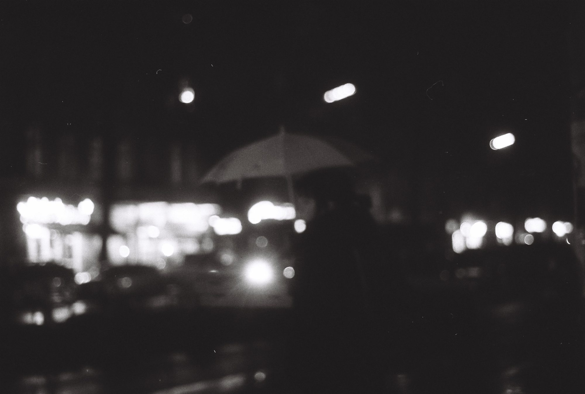 Out-of-focus night street, a figure under an umbrella against glowing shop lights