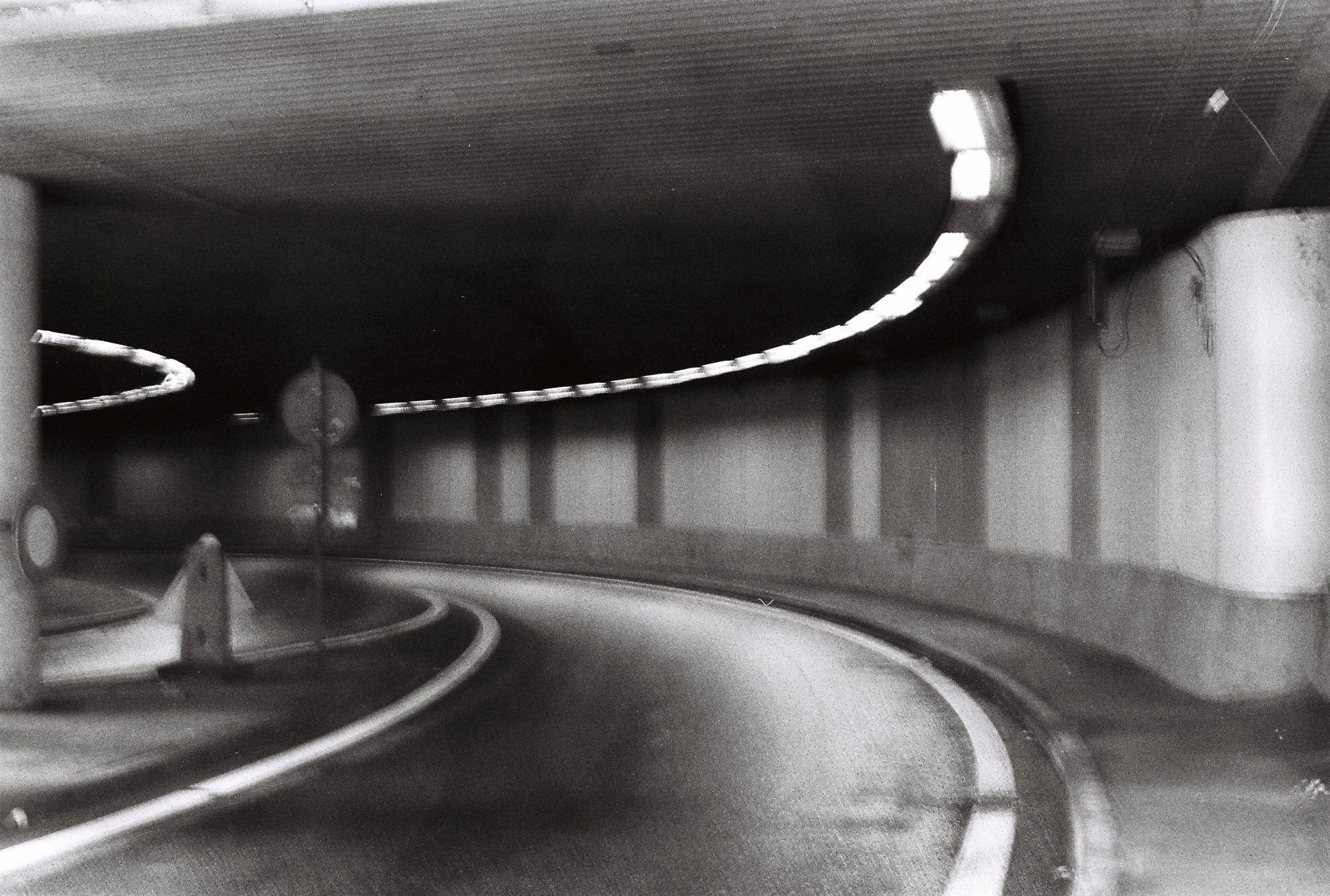 Black and white curving road through an empty concrete tunnel, ceiling lights following the bend