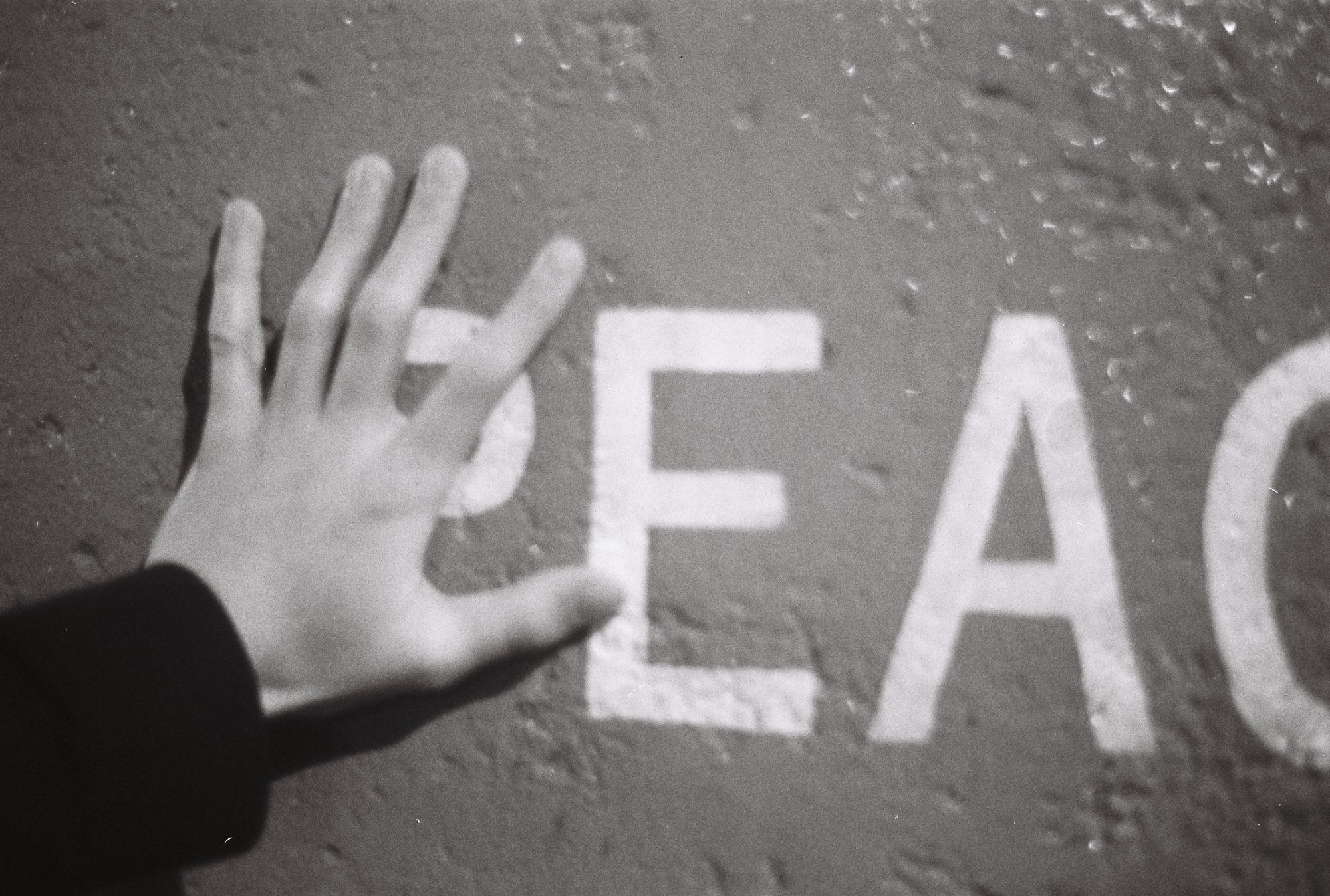 A hand pressed against a wall painted with the word PEACE