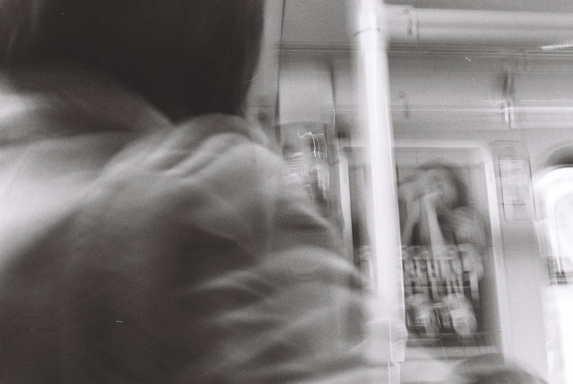 Motion blur inside a train carriage, a passenger in a hooded jacket beside a pole