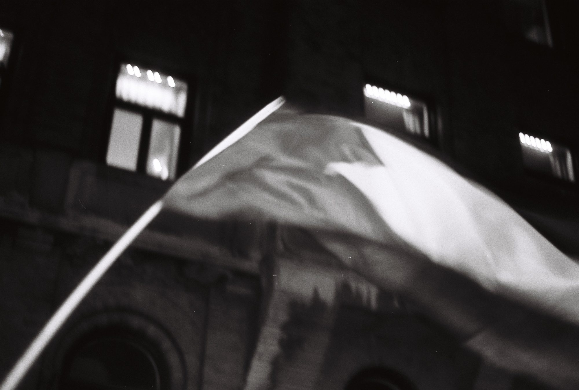 A flag sweeping across the frame in front of a lit building facade at night