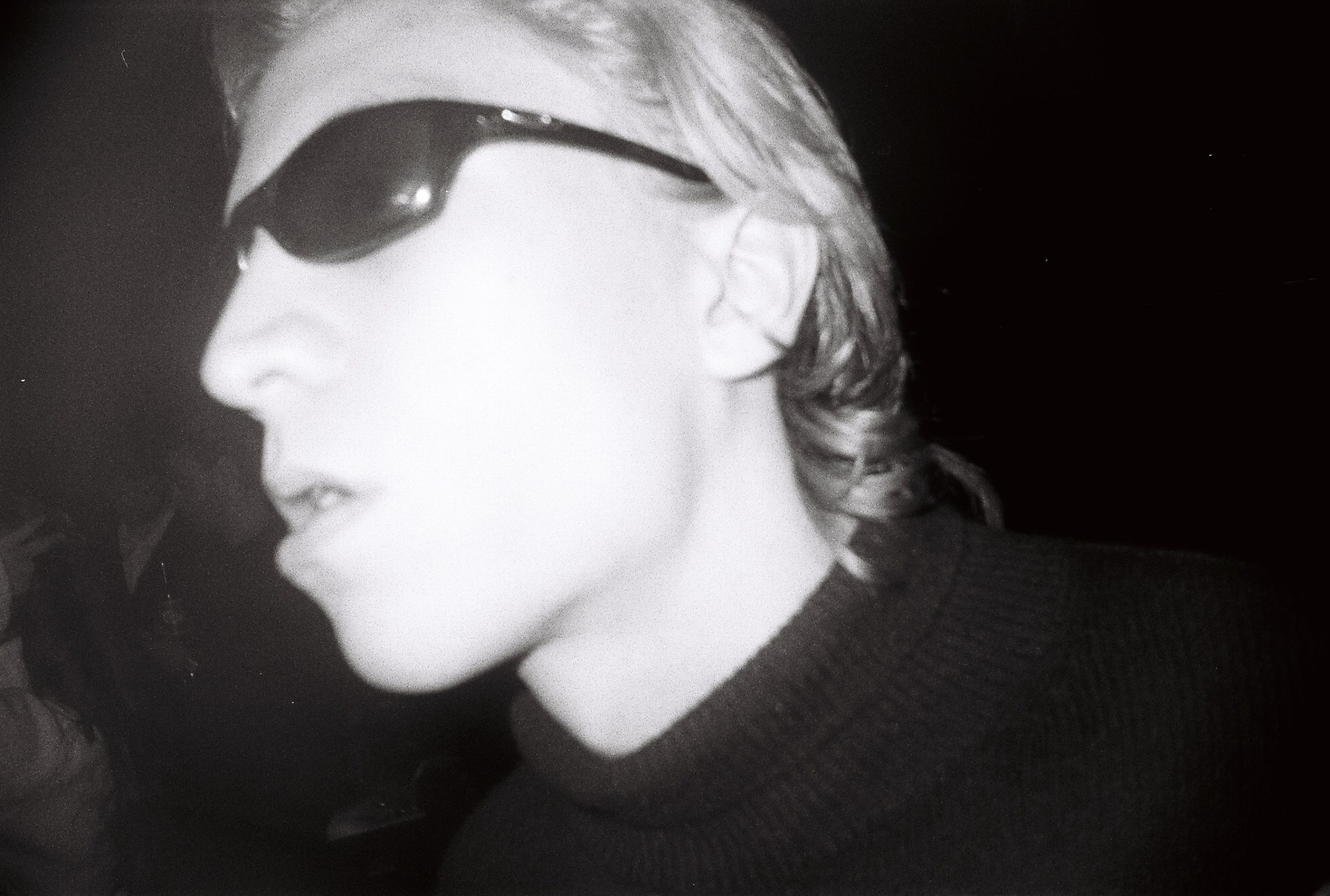 Flash portrait in profile of a person in dark sunglasses and a knit sweater