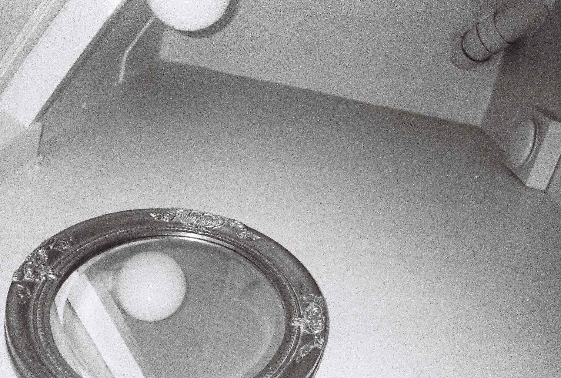 An ornate round mirror on a pale floor reflecting a globe lamp
