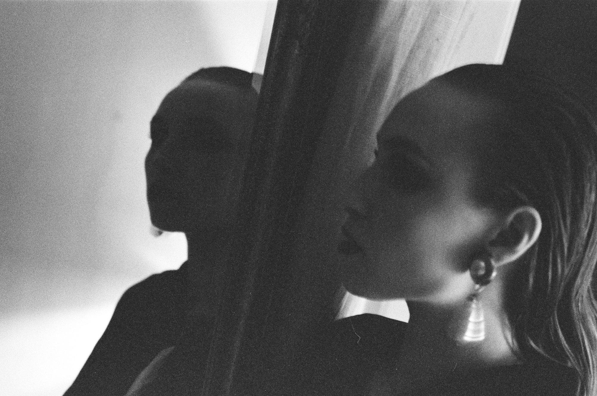 Portrait of a woman in profile with a drop earring, a second figure in shadow behind a curtain