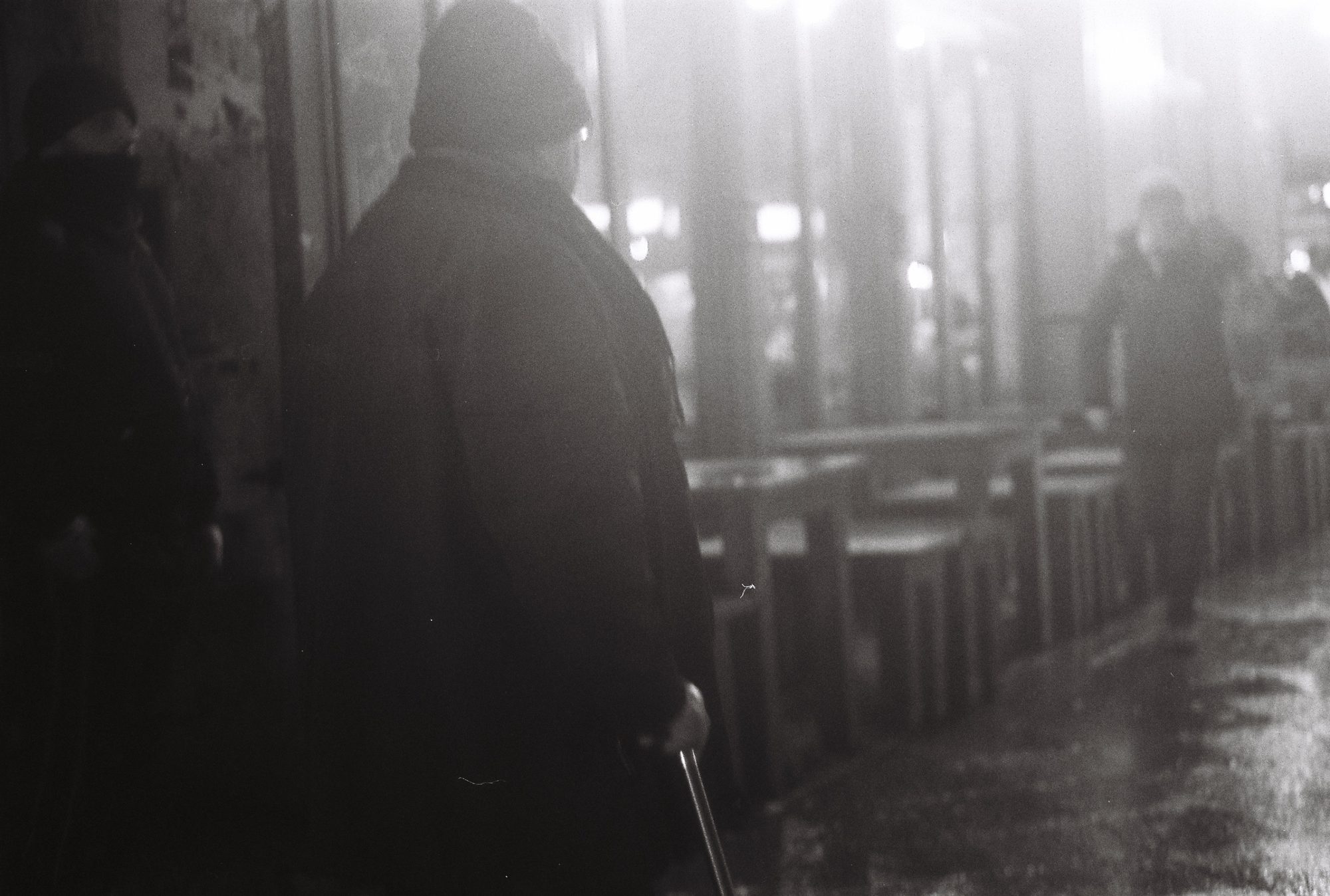 A man in a long coat with a cane on a misty night street