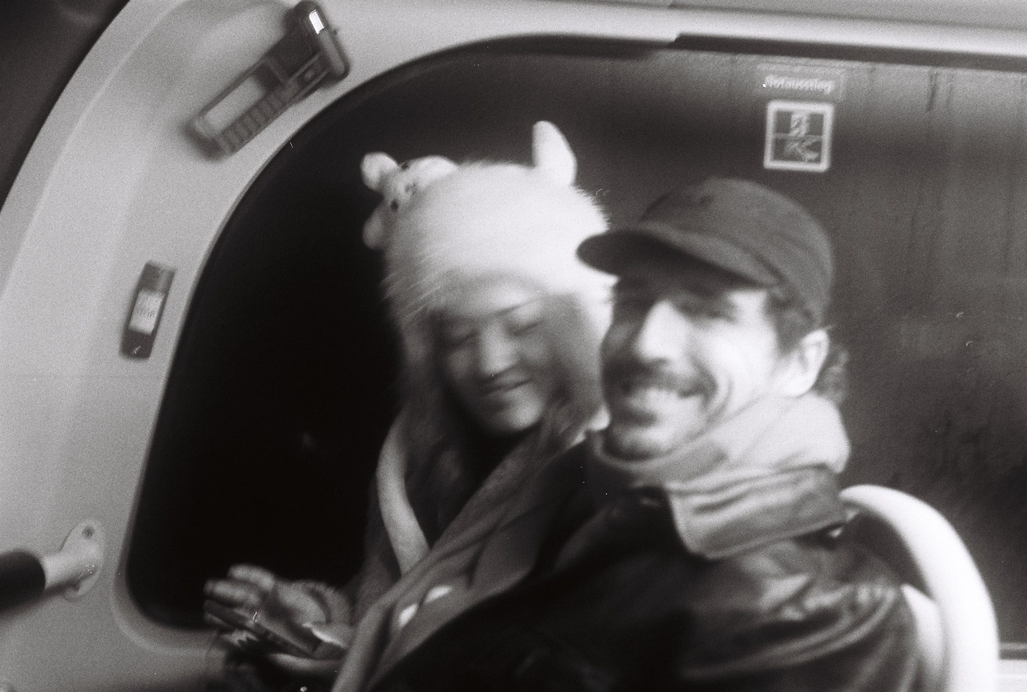 Two smiling passengers on a train, one in a fluffy hat with ears