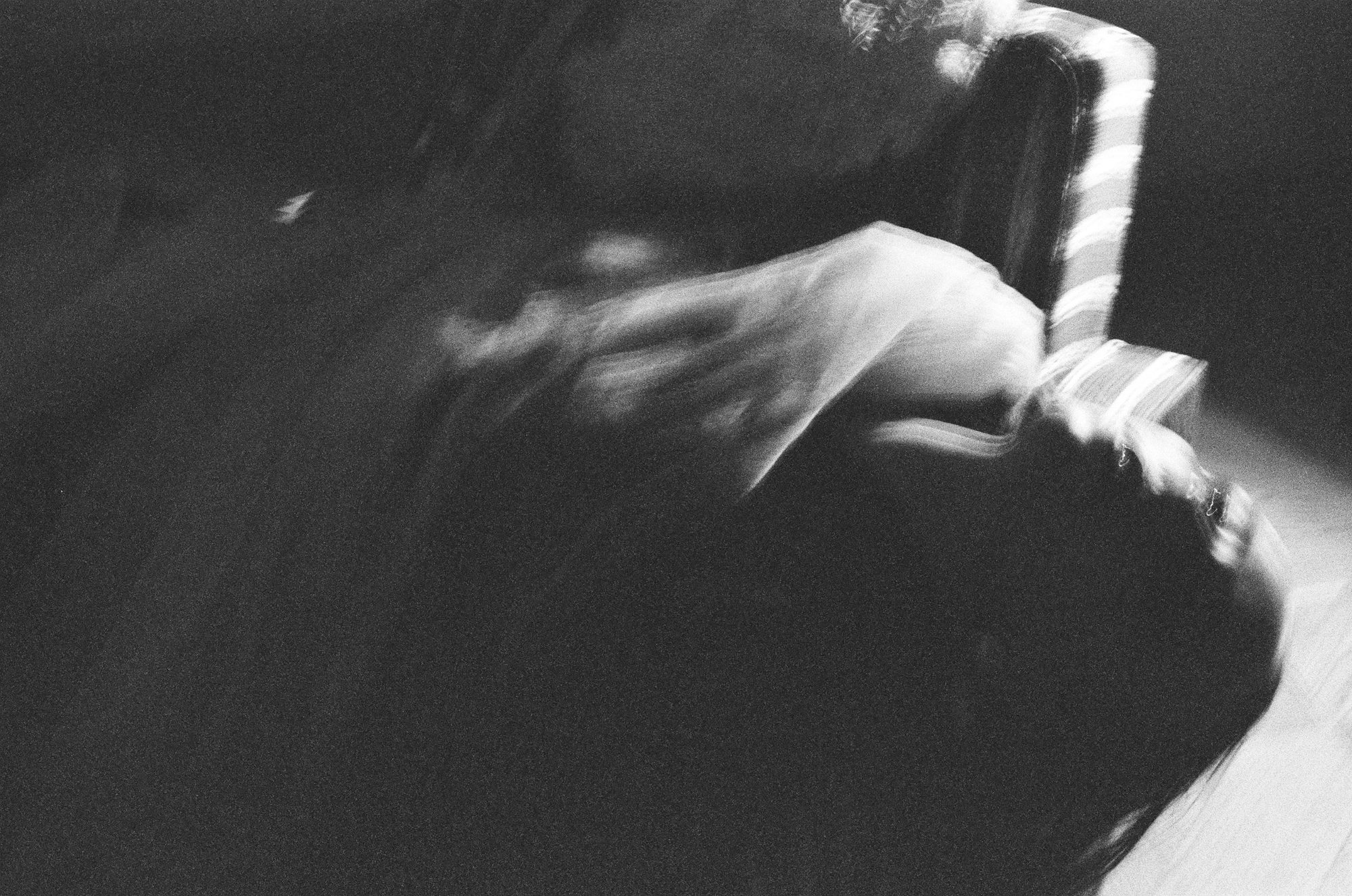 A figure in a white dress spinning in motion blur beside a striped armchair