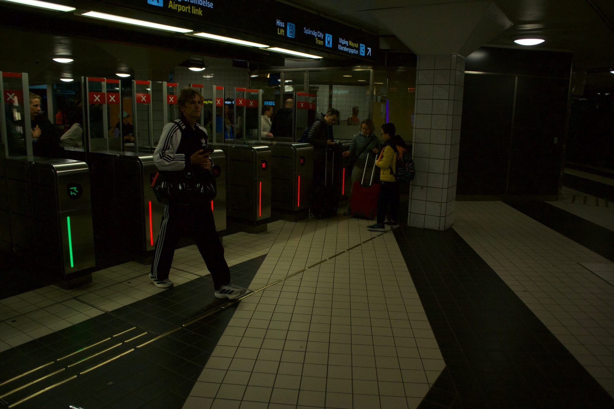 A man in a tracksuit walking past metro ticket gates lit red and green