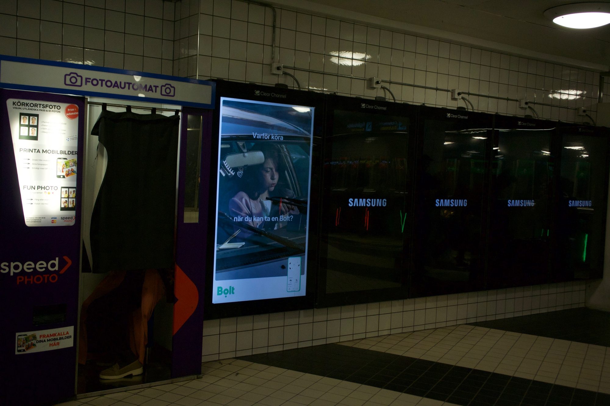 A photo booth beside glowing advertising screens in a tiled metro passage
