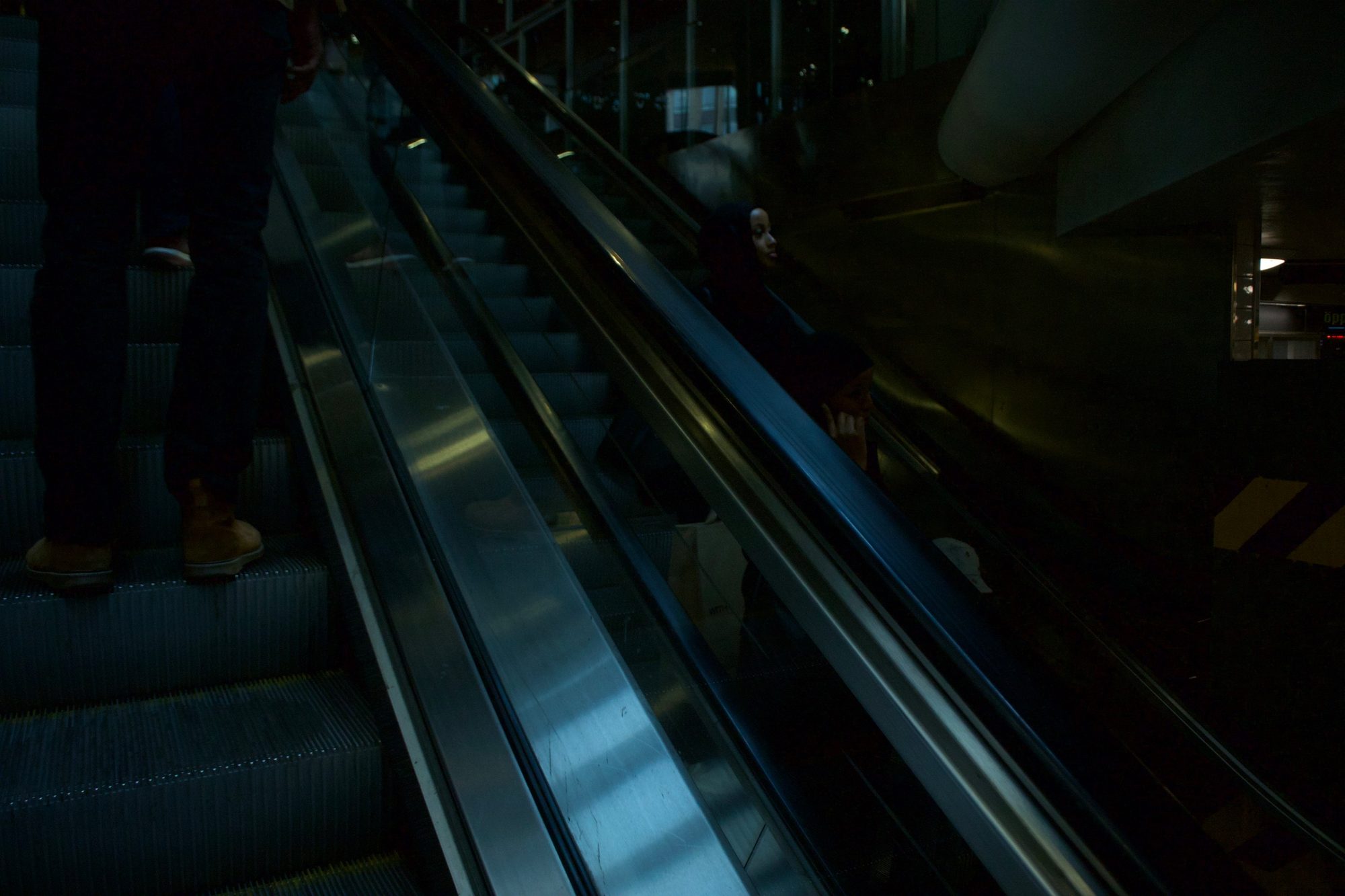 Dark escalators in blue light, two people riding down