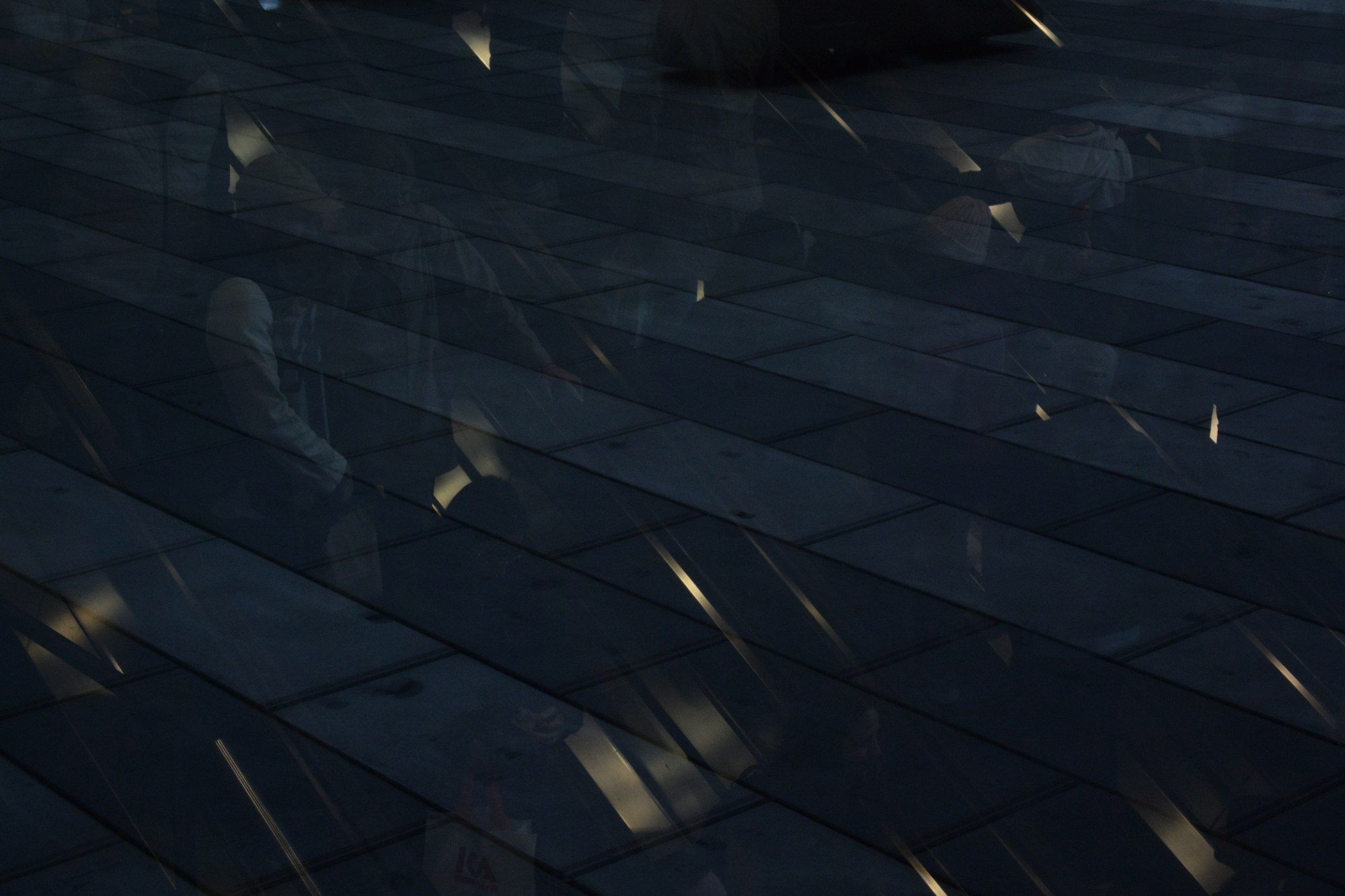 Ghostly reflections of passers-by over dark paving stones
