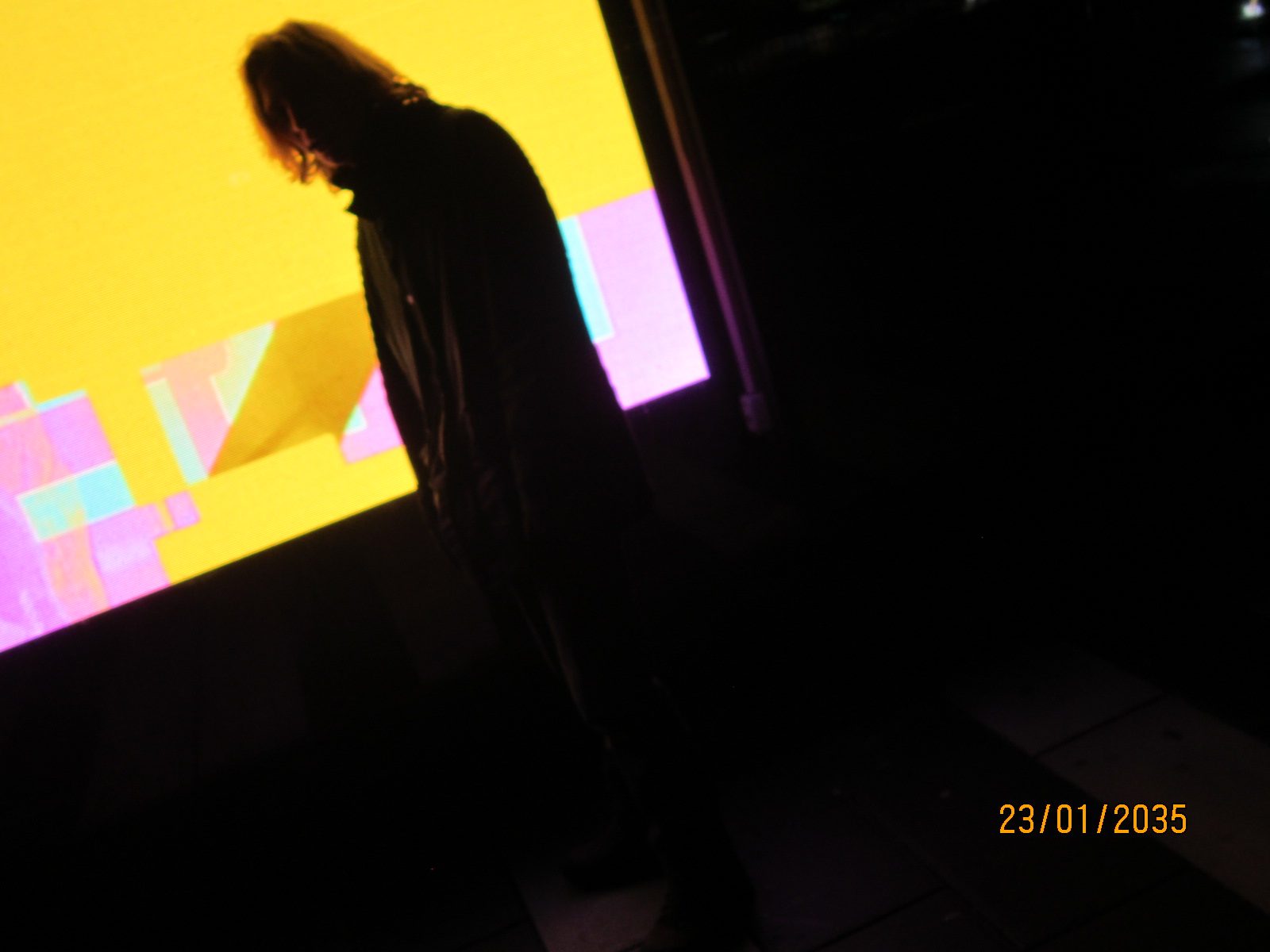 A silhouette with head bowed against a bright yellow and pink screen