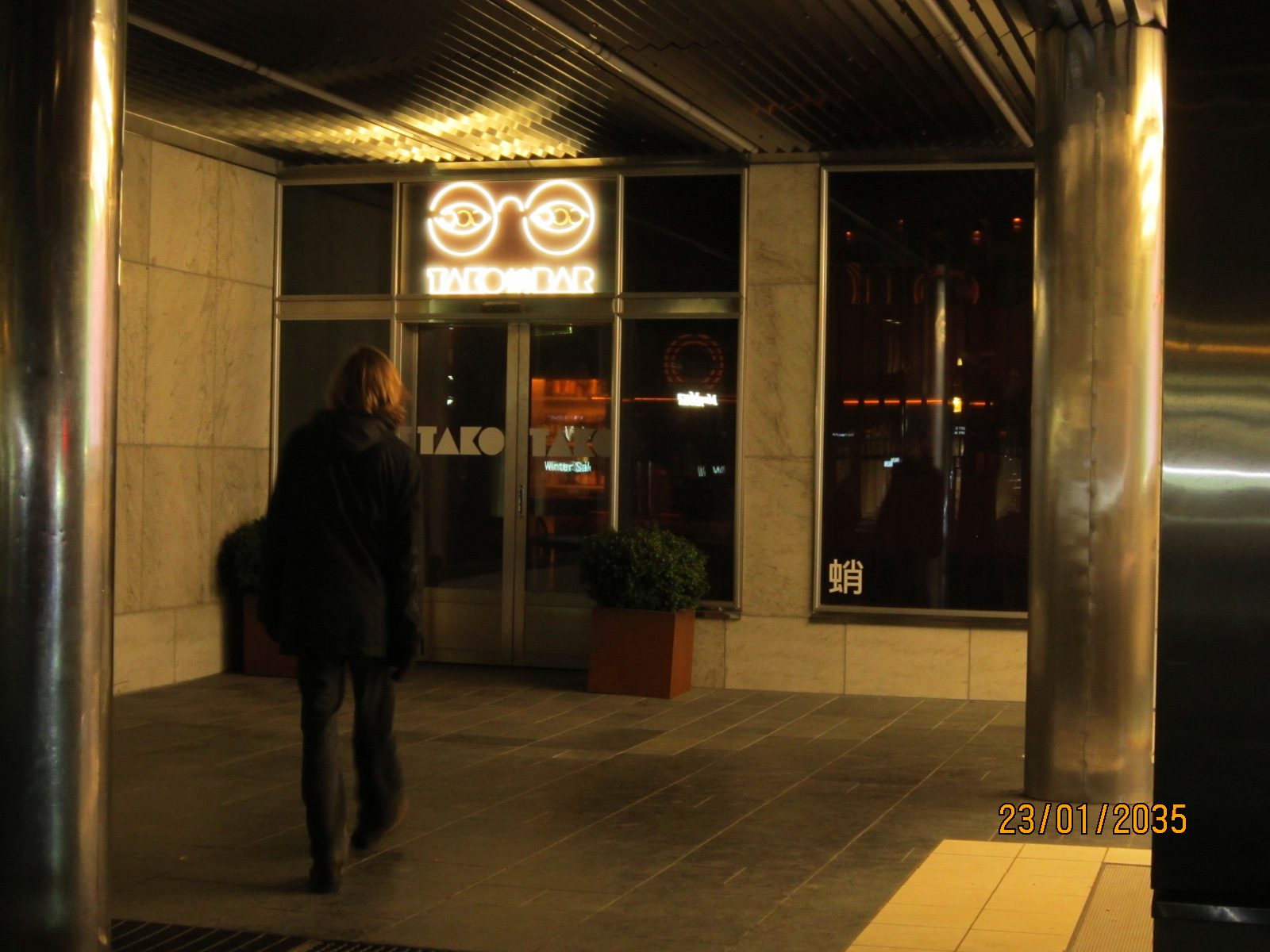 A figure walking towards a bar entrance with a glowing sign
