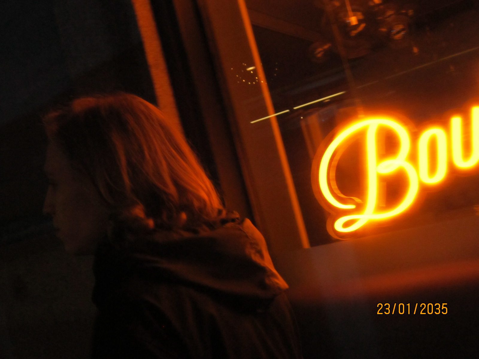 A profile with long hair lit orange beside a neon script sign