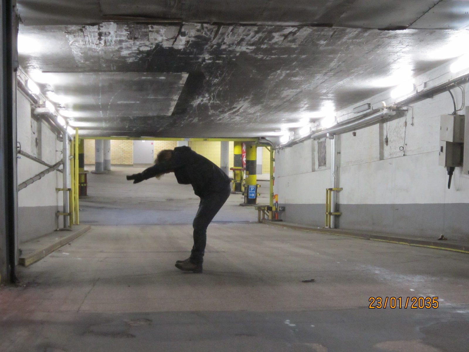 A figure bent forward with arms stretched out in an empty underground car park