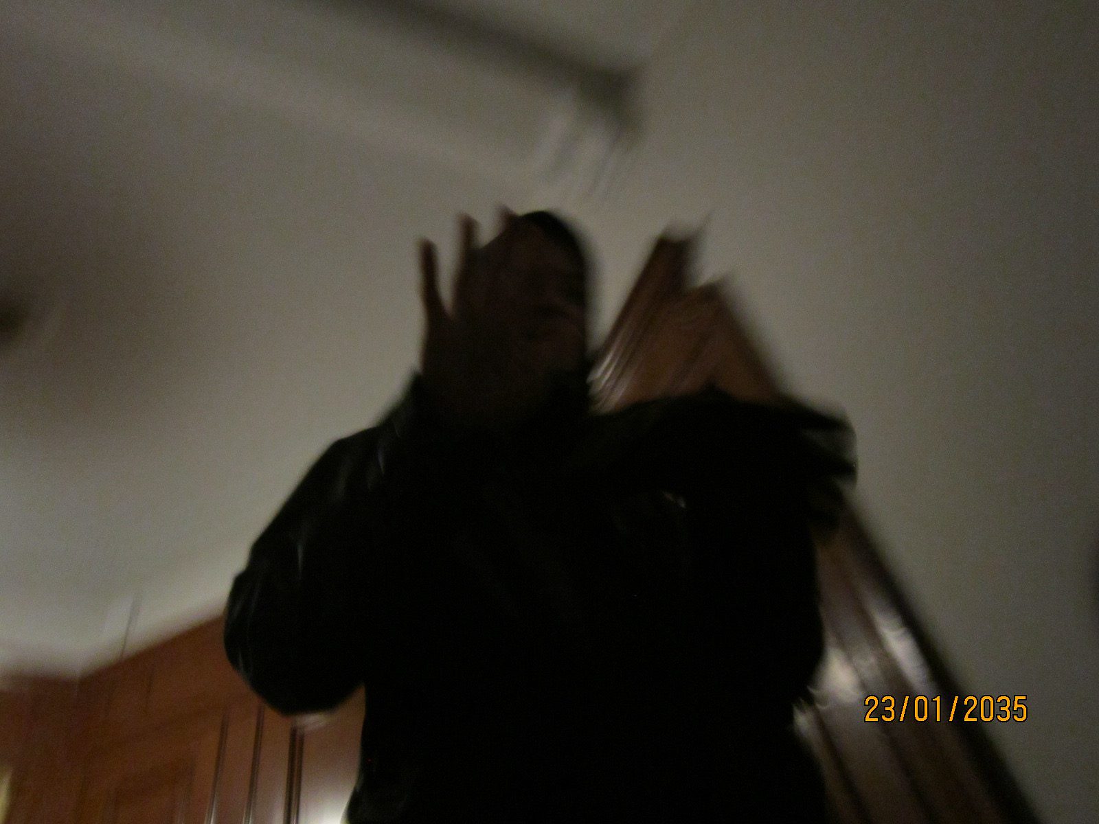 A dark figure in motion seen from below, hands blurred against a pale ceiling