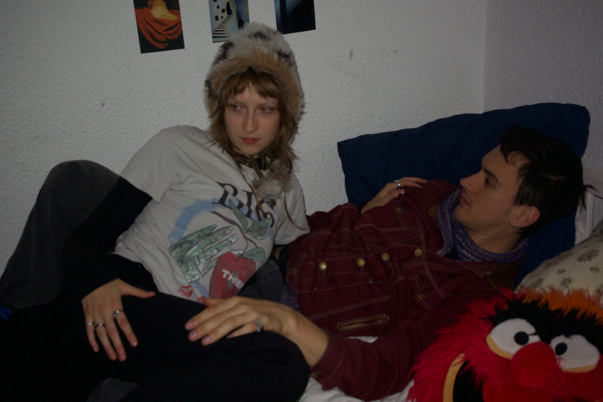 The couple resting on the bed, she glances at the camera while he looks at her