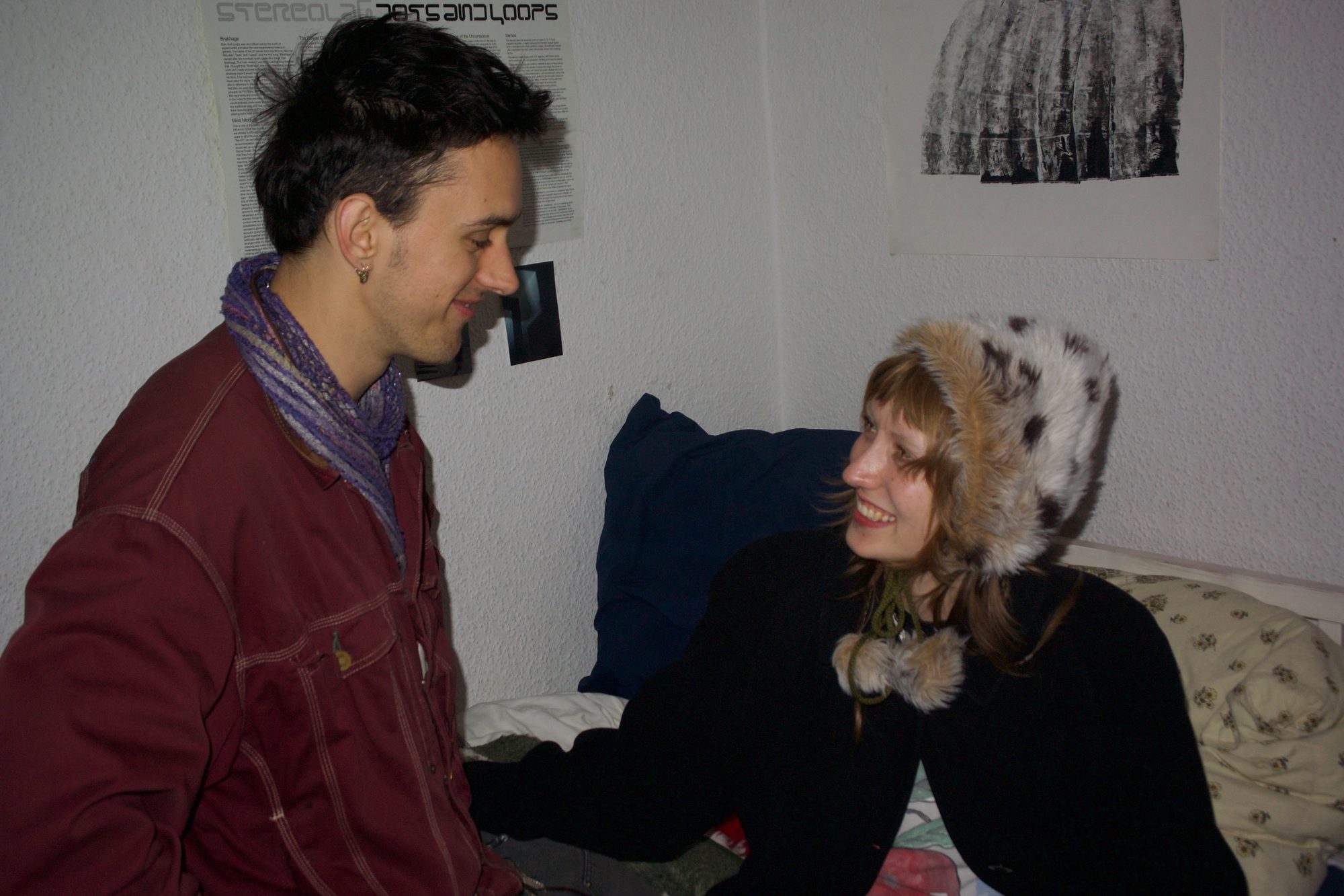 He stands smiling down at her as she looks up from the bed in a fur hat